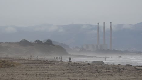 Morro-Bay-Smokestacks-Or-Stacks-In-Distance-With-People-Walking-On-Beach