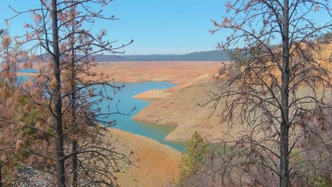 Rising-Aerial-Over-Drought-Stricken-California-Lake-Oroville-With-Low-Water-Levels,-Receding-Shoreline-And-Burned-Trees-And-Forests