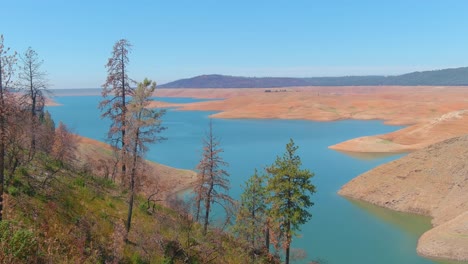 Disturbing-Aerial-Over-Drought-Stricken-California-Lake-Oroville-With-Low-Water-Levels,-Receding-Shoreline-And-Burned-Trees-And-Forests