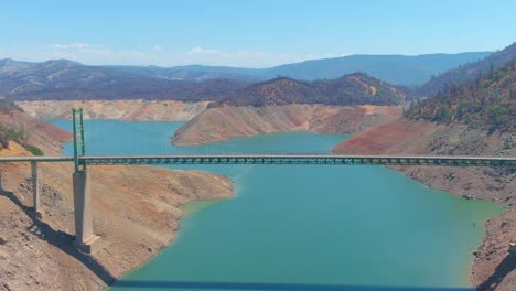Inquietante-Antena-Sobre-El-Lago-Oroville-De-California-Azotado-Por-La-Sequía-Con-Bajos-Niveles-De-Agua,-Costa-En-Retroceso-Y-Gran-Cruce-De-Puentes