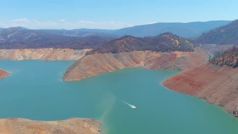 Störende-Luft-über-Dem-Von-Dürre-Betroffenen-Kalifornischen-Oroville-See-Mit-Niedrigem-Wasserstand,-Zurückweichender-Küstenlinie-Und-Booten-Im-Niedrigwasser