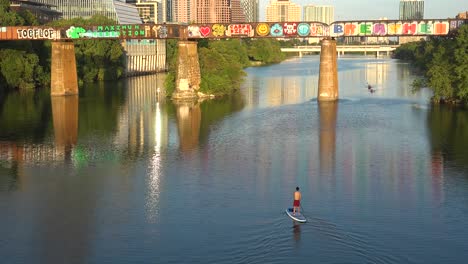 A-Paddleboarder-Rows-Down-The-Colorado-River-As-The-Skyline-Of-Downtown-Austin-Texas-Is-Revealed