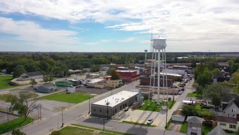 Aerial-Establishing-Shot-Over-Main-Street-Small-Town-Usa-With-Water-Tower-And-Freight-Train-Passing-Background