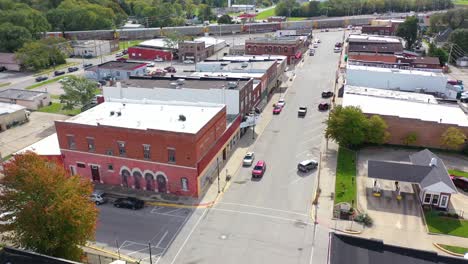 Aerial-Establishing-Shot-Over-Main-Street-Small-Town-Usa-With-Water-Tower-And-Freight-Train-Passing-Background