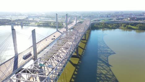 Antena-Sobre-Los-Puentes-Del-Río-Ohio-Con-El-Horizonte-Del-Centro-De-Louisville,-Kentucky-Distante-Sugiere-Infraestructura