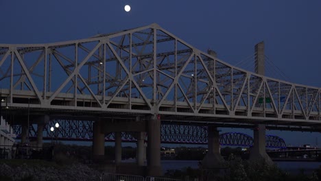Toma-Nocturna-De-Establecimiento-De-Puentes-Sobre-El-Río-Ohio-En-Jeffersonville,-Indiana-Y-Louisville,-Kentucky,-Con-La-Luna-Visible