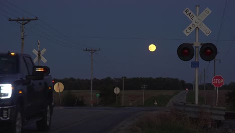 A-Pickup-Truck-Crosses-A-Railroad-Crossing-With-A-Full-Moon-In-The-Distance-At-Night
