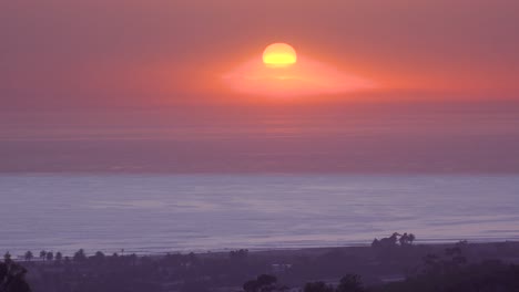 Time-Lapse-Of-A-Huge-Red-Round-Ball-Of-Sun-Setting-At-Sunset-Over-The-Pacific-Ocean-Near-Malibu,-California