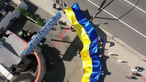 Ukrainische-Demonstranten-Von-Oben-Nach-Unten-Mit-Großer-Ukrainischer-Flagge-Protestieren-Gegen-Die-Russische-Invasion-Ihres-Landes,-Auf-Der-Straße-In-Malibu,-Kalifornien,-Mit-Malibu-Schild