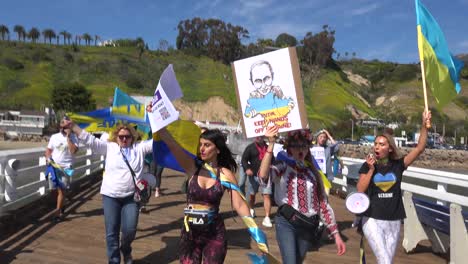 Ukrainische-Antikriegs-Demonstranten-Singen-Und-Marschieren-Auf-Dem-Malibu-Pier-Mit-Schildern-Und-Fahnen,-Um-Gegen-Die-Russische-Invasion-In-Der-Ukraine-Zu-Protestieren