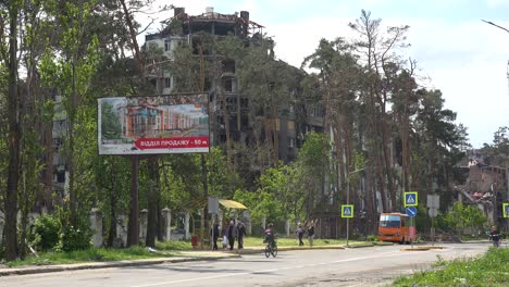 People-Walk-In-A-Devastated-Neighborhood-Of-Irpin,-Kiev,-Where-A-Billboard-Advertises-A-Better-Future