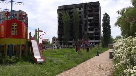 Niños-En-Columpios-En-El-Patio-De-Recreo-En-Borodianka,-Borodyanka,-Ucrania-Con-Edificios-De-Apartamentos-Bombardeados-Y-Disparados-Con-Cohetes-Donde-Cientos-Fueron-Asesinados-Por-La-Ocupación-Rusa