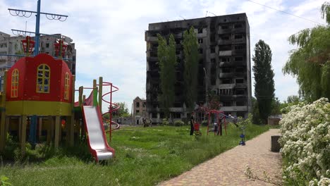 Kids-On-Swings-On-Playground-In-Borodianka,-Borodyanka,-Ukraine-With-Bombed-And-Rocketed-Apartment-Buildings-Where-Hundreds-Were-Killed-By-Russian-Occupation