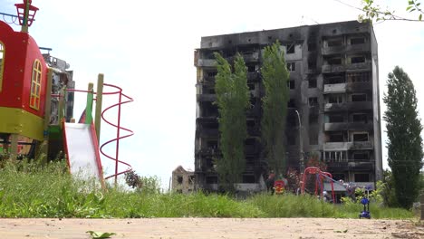 Kids-On-Swings-On-Playground-In-Borodianka,-Borodyanka,-Ukraine-With-Bombed-And-Rocketed-Apartment-Buildings-Where-Hundreds-Were-Killed-By-Russian-Occupation