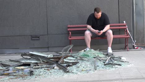 Ordinary-Man-On-The-Street-In-Ukraine-Texts-Friends-Near-A-Large-Pile-Of-Glass-And-Debris