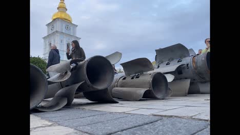 Ukrainians-Admire-Russian-Bombs-And-Other-War-Wreckage-Sitting-In-A-Square-In-Downtown-Kyiv,-Kiev-Ukraine