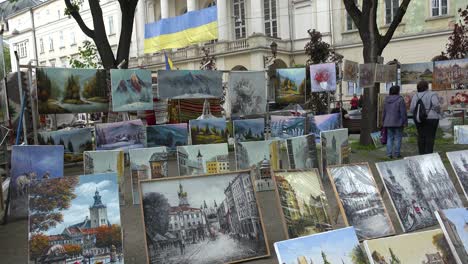 Obras-De-Arte-Y-Pinturas-En-Una-Feria-De-Artes-Y-Oficios-En-Lviv,-Ucrania-Con-Edificios-Públicos-Y-Fondo-De-Bandera