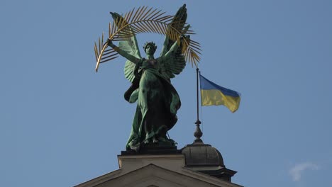 The-Ukrainian-Flag-Flies-With-A-Majestic-Statue-On-Top-Of-The-Opera-House-In-Lviv,-Ukraine
