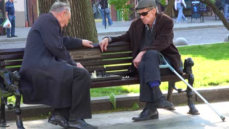 Two-Old-Men-Play-Chess-On-A-Bench-In-The-Park-In-Central-Lviv,-Ukraine
