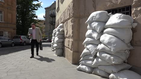 A-Businessman-Walks-Along-A-Street-In-Lviv,-Ukraine-With-Sandbags-Stacked-Against-Windows-During-The-War-In-Ukraine