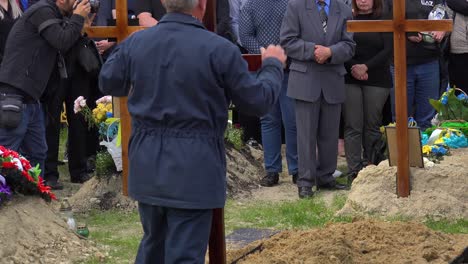 Ein-Christliches-Kreuz-Markiert-Die-Grabstätte-Eines-Gefallenen-Ukrainischen-Soldaten-Während-Des-Krieges-In-Der-Ukraine,-Die-Familie-Schaut-Zu