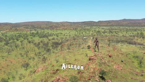 Hervorragende-Luftaufnahme-Des-Querruderzeichens-In-Australien-Mit-Einer-Riesigen-Statue-Eines-Ureinwohners-Dahinter