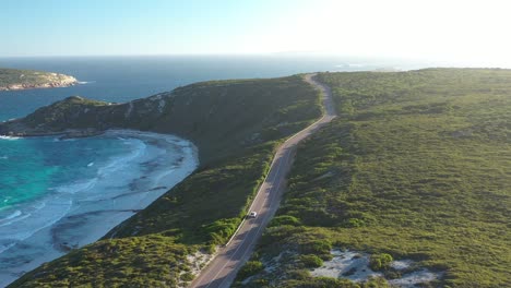 Excellent-Aerial-Shot-Of-Cars-Driving-Along-Great-Ocean-Drive-In-Esperance,-Australia-As-Waves-Lap-The-Beach