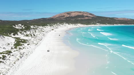 Excellent-Aerial-Shot-Of-Cars-Driving-On-The-White-Sands-Of-Wharton-Bay-As-Clear-Blue-Water-Laps-The-Shore-In-Esperance,-Australia