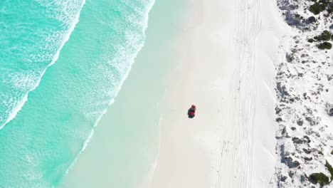 Excellent-Aerial-Shot-Of-A-Truck-Driving-On-The-White-Sands-Of-Wharton-Bay-As-Clear-Blue-Water-Laps-The-Shore-In-Esperance,-Australia