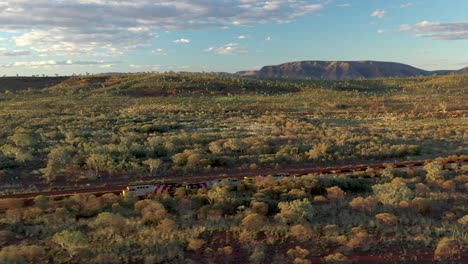 Excellent-Aerial-Shot-Of-A-Coal-Train-Traveling-Past-Shrubs-And-Mountains-In-Tom-Price,-Australia