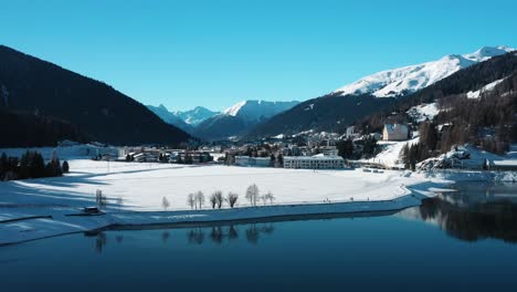 Excellent-Aerial-View-Approaching-Snowy-Davos,-Switzerland-Over-A-Lake