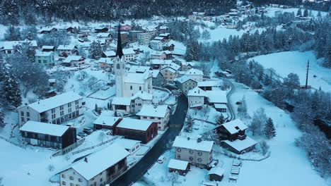Excellent-Aerial-View-Of-A-Car-Driving-Past-A-Chapel-In-Wintry-Filisur,-Switzerland
