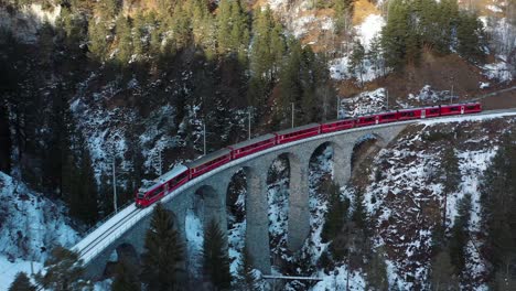 Ausgezeichnete-Luftaufnahme-Eines-Zuges,-Der-über-Die-Brücke-Einer-Schneebedeckten-Bergregion-Der-Schweiz-Fährt