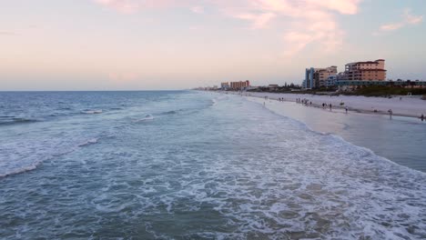 Excellent-Aerial-View-Of-People-Walking-Along-The-Shore-Of-New-Smyrna-Beach,-Florida-At-Dusk
