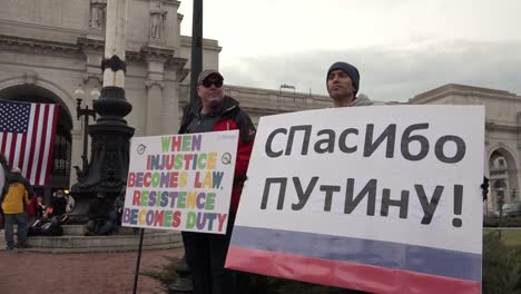 Zwei-Männliche-Politische-Demonstranten-Tragen-Ein-Schild,-Eines-In-Russischer-Sprache,-Das-Gegen-Den-Gewählten-Präsidenten-Donald-Trump-Protestiert