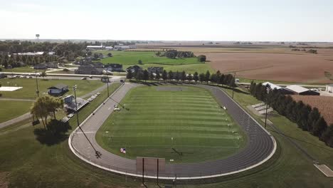 Aerial-Drone-Footage-Of-High-School-Football-Field-And-Tall-Brown-Fields-Ready-For-Harvest-In-Rural,-Midwest-Iowa-Corn-Country