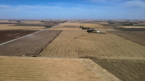 Aerial-Drone-Footage-Brown,-Dry,-Corn-Fields,-Farmland-And-Sustainable-Windmills,-Under-Blue-Skies-Rural,-Midwestern-Iowa