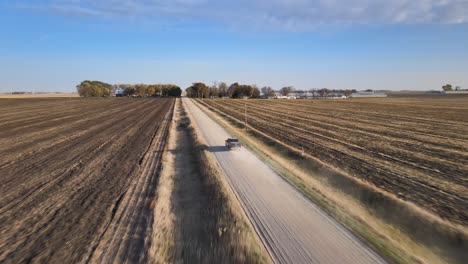 Aerial-Drone-Following-Shot-Of-A-Pickup-Truck-Driving-On-A-Dusty,-Gravel-Road-Under-Blue-Skies-In-Rural,-Midwestern,-Iowa