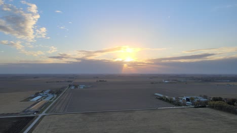Drohnenaufnahmen-Aus-Der-Luft-Bei-Sonnenuntergang-Eines-Autos,-Das-Eine-Staubwolke-Auf-Einer-Ländlichen-Schotterstraße-In-Iowa-Farm-Country-Aufwirbelt