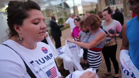 Ein-Junger-Mann-Und-Eine-Junge-Frau-Verteilen-Trump-t-shirts-An-Wähler-Und-Seine-Unterstützer-Außerhalb-Einer-Wahlkampfveranstaltung-In-Iowa-Während-Seiner-Präsidentschaftswahl