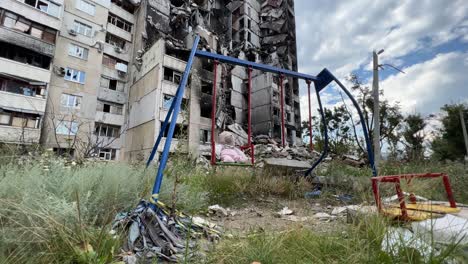 Ein-Spielplatz-Mit-Einem-Teddybären-Auf-Einer-Schaukel-Und-Gebäude-Werden-Durch-Russische-Luftangriffe-In-Der-Region-Saltivka-In-Charkiw,-Ukraine,-Zerstört