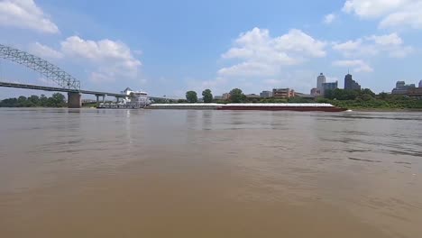 A-Commercial-Barge-Travels-Down-The-Mississippi-River-In-Front-Of-The-Skyline-Of-Memphis-Tennessee