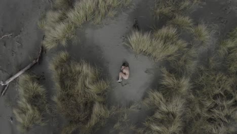 Excellent-Aerial-Shot-Zooming-Out-From-A-Naked,-Tattooed-Woman-Curled-Up-On-The-Beach