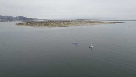Vuelo-Aéreo-Sobre-Dos-Paddle-Boarders-En-Morro-Bay,-California-En-Un-Día-Nublado