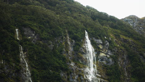 Aerial-panning-view-of-little-waterfall-that-runs-along-the-ridge-of-mountain