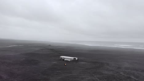 Zoom-out-aerial-of-a-white-plane-wreck-on-a-black-beach-in-Iceland