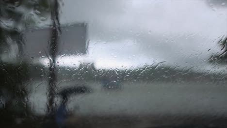 Blick-Aus-Einem-Mit-Wassertröpfchen-Bedeckten-Fenster,-Um-Eine-Person-Zu-Sehen,-Die-Im-Strömenden-Regen-Entlang-Des-Mandovi-Flusses,-Panjim,-Indien,-Unter-Einem-Regenschirm-Sitzt