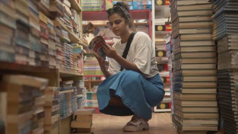 A-slow-motion-shot-of-an-attractive-Asian-female-flicking-through-the-pages-of-a-book-while-on-her-haunches-in-the-isle-of-a-bookstore,-India