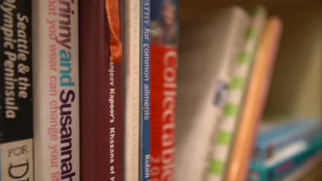 A-closeup-dolly-shot-tracking-along-a-library-bookshelf,-the-titles-visible-on-the-spine-of-the-respective-books