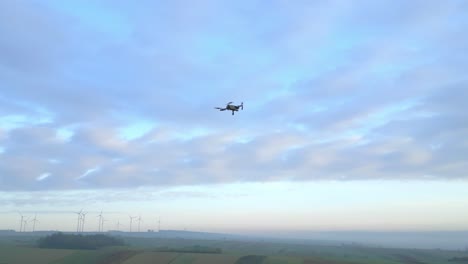 Drone-Filming-A-Drone-Flying-Against-Sky-With-Clouds-Over-Rural-Landscape-At-Dusk